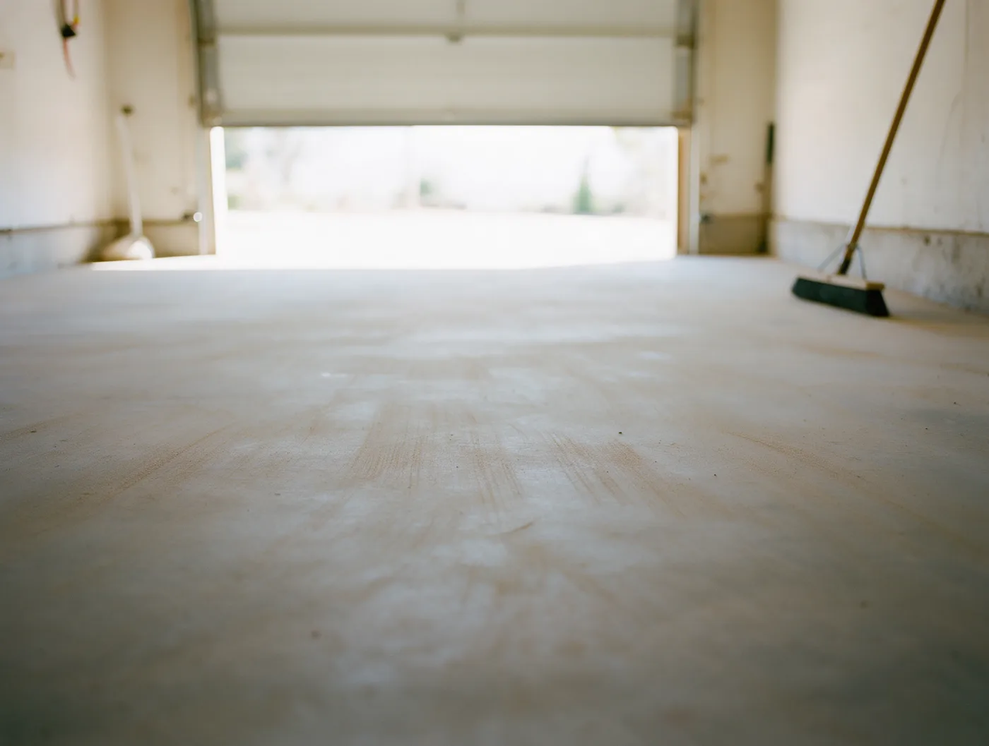 A swept, completely empty concrete garage floor with a broom against the wall